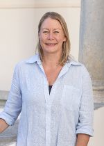 Eine Dame mit blonden halblangem Haar und einer hellblaufarbenen Leinenbluse
