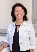 Dame mit weißer Jacke und dunklen, mittellangen Haaren vor hellgrauem Hintergrund
