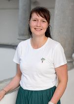 Frau mit langen dunklen Haaren mit Stirnfransen im weißem Shirt vor hellgrauem Hintergrund